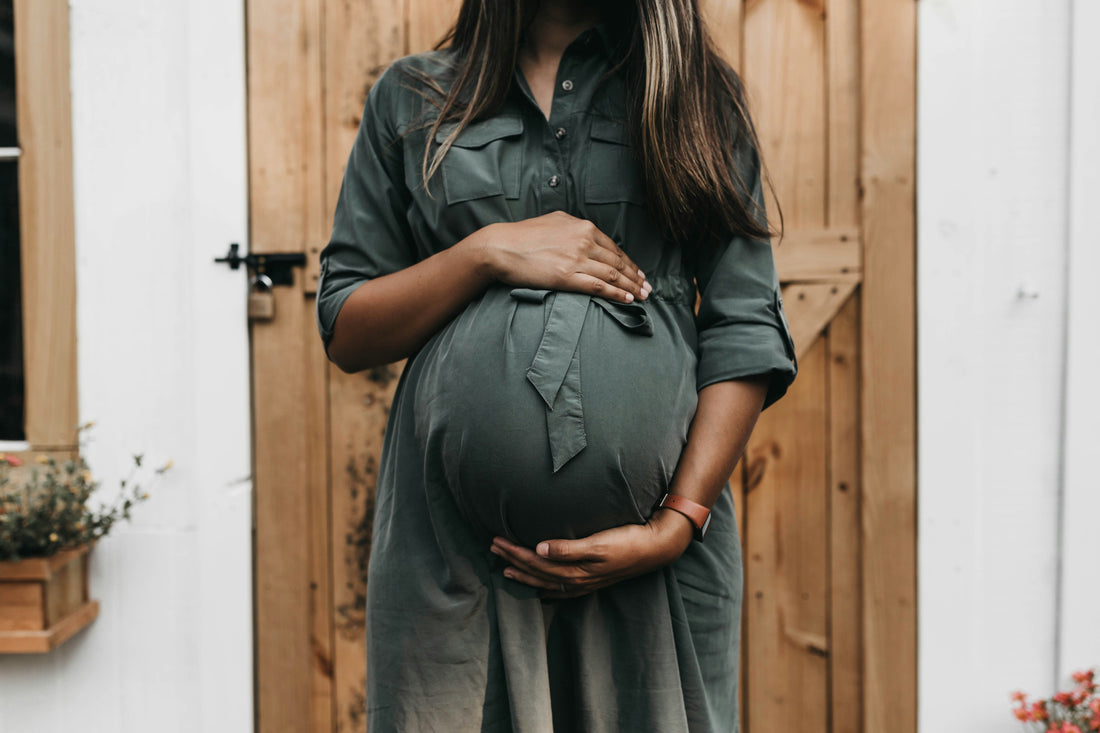 Woman in a green maternity dress cradling her baby bump, illustrating the Maternity Dress Guide.